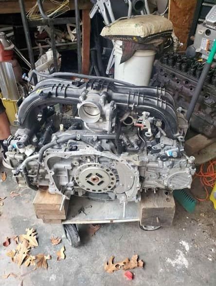 A subaru engine is sitting on top of a wooden pallet in a garage.