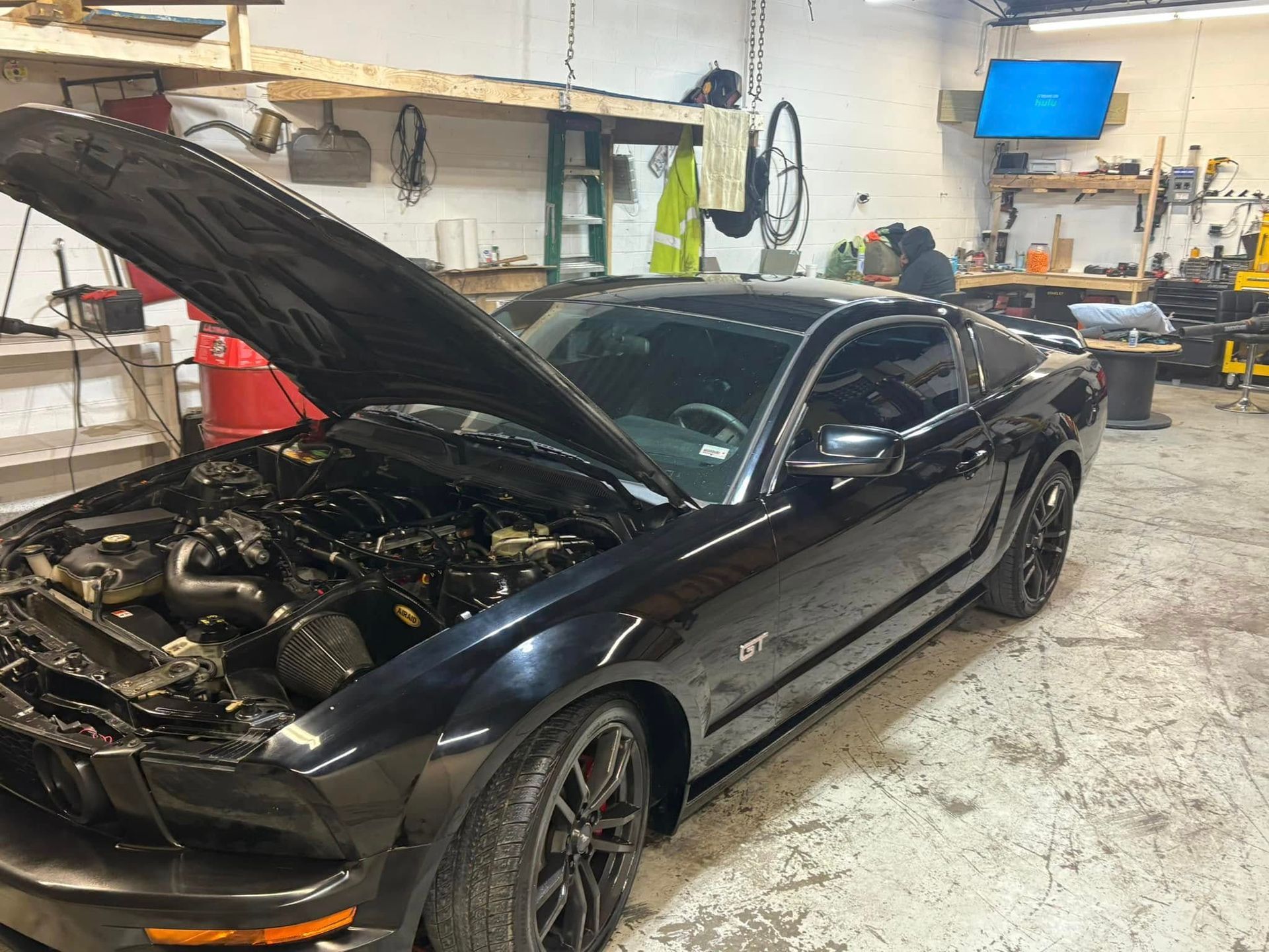 A black mustang with its hood open is parked in a garage.
