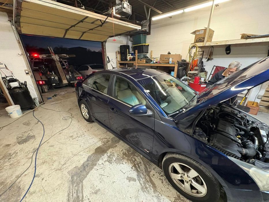 A blue car with its hood open is parked in a garage.