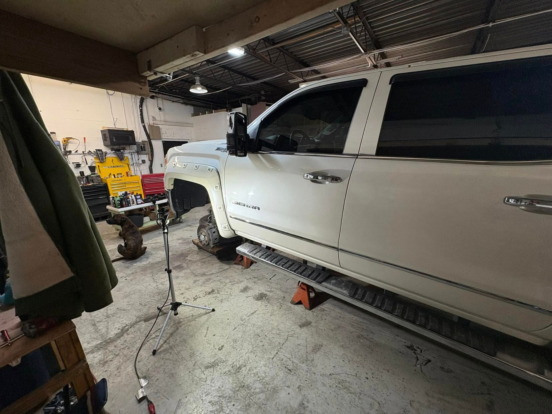 A white truck is sitting on a jack in a garage.