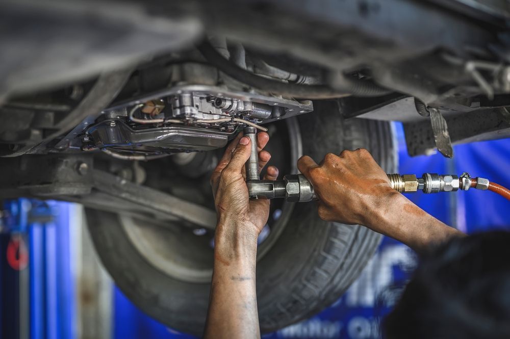 A man is working on the underside of a car in a garage.