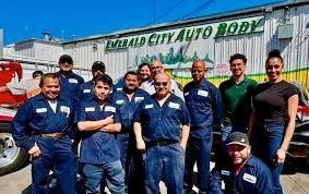 A group of people are posing for a picture in front of a building that says emerald city auto body