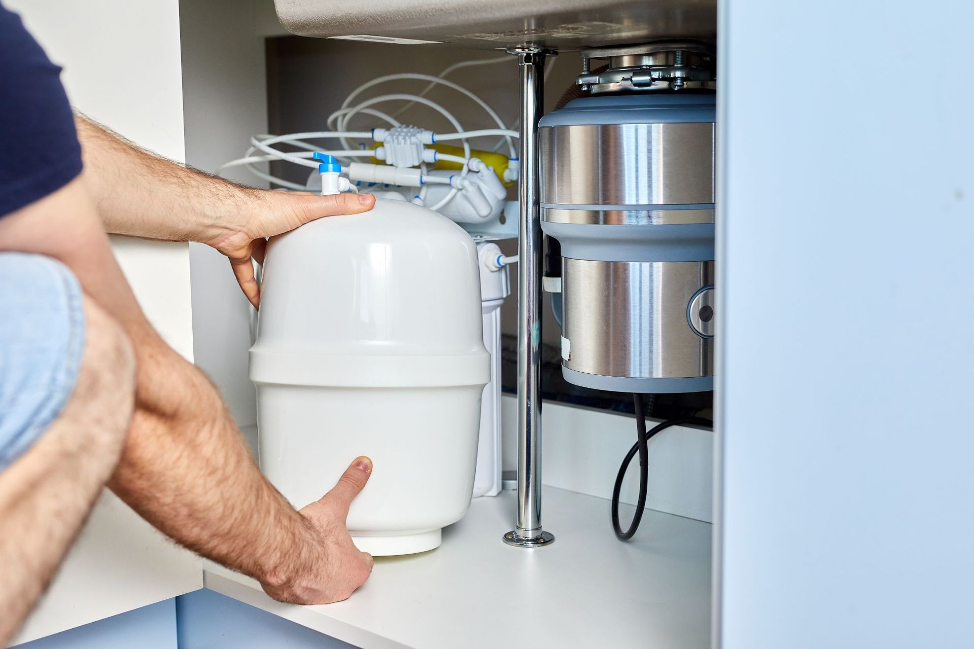 Person installs a water filter under a kitchen sink, near a garbage disposal.