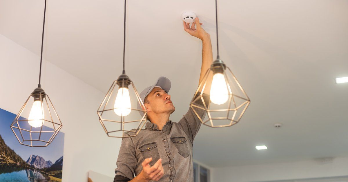 A handyman reaches up to the ceiling to replace the smoke alarm battery.