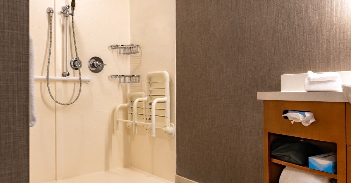 An ADA-compliant home bathroom freshly remodeled. The shower is curbless with a pull-down bench attached to the wall.