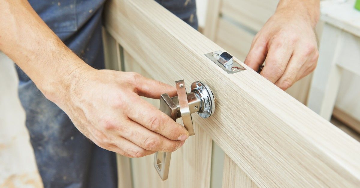 A close-up of a door on its side, off the hinges, as a home handyman changes the handle and locking mechanism.
