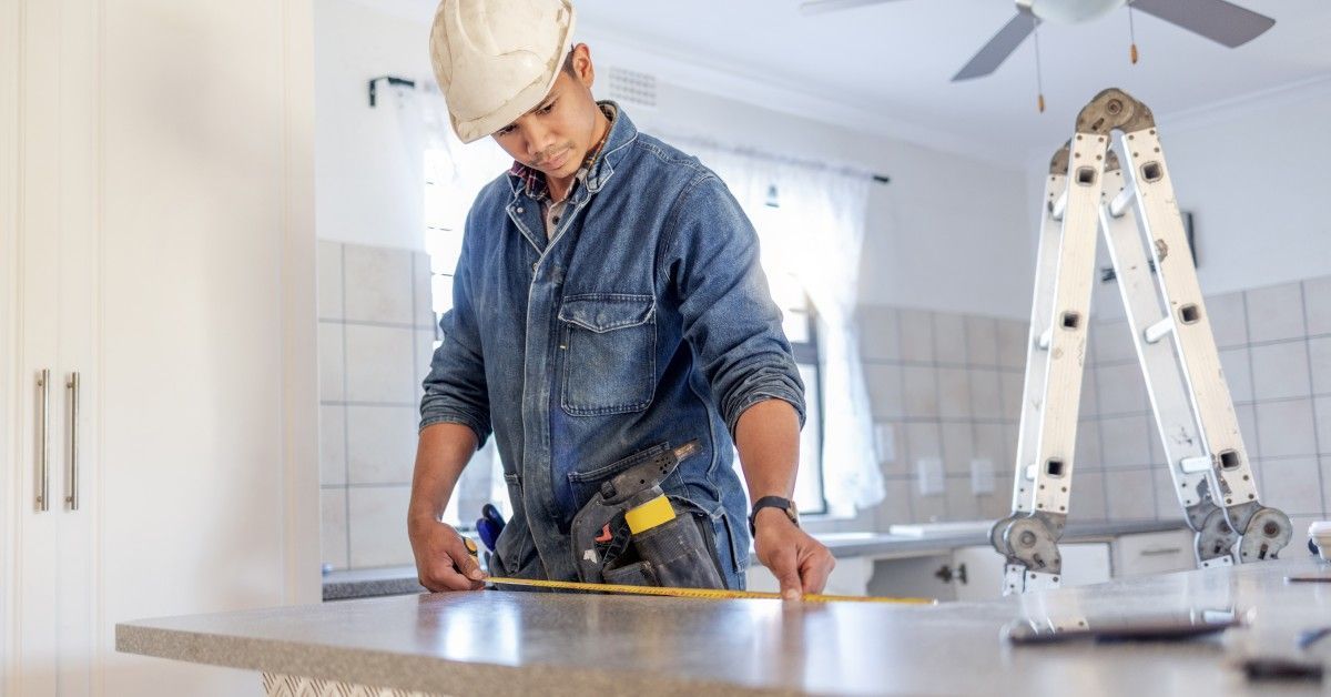 A handyman stands at the kitchen island with a white hard hat and a denim shirt.