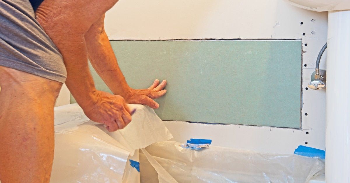 A homeowner stands next to a patch of newly set drywall that still needs patched and painted.