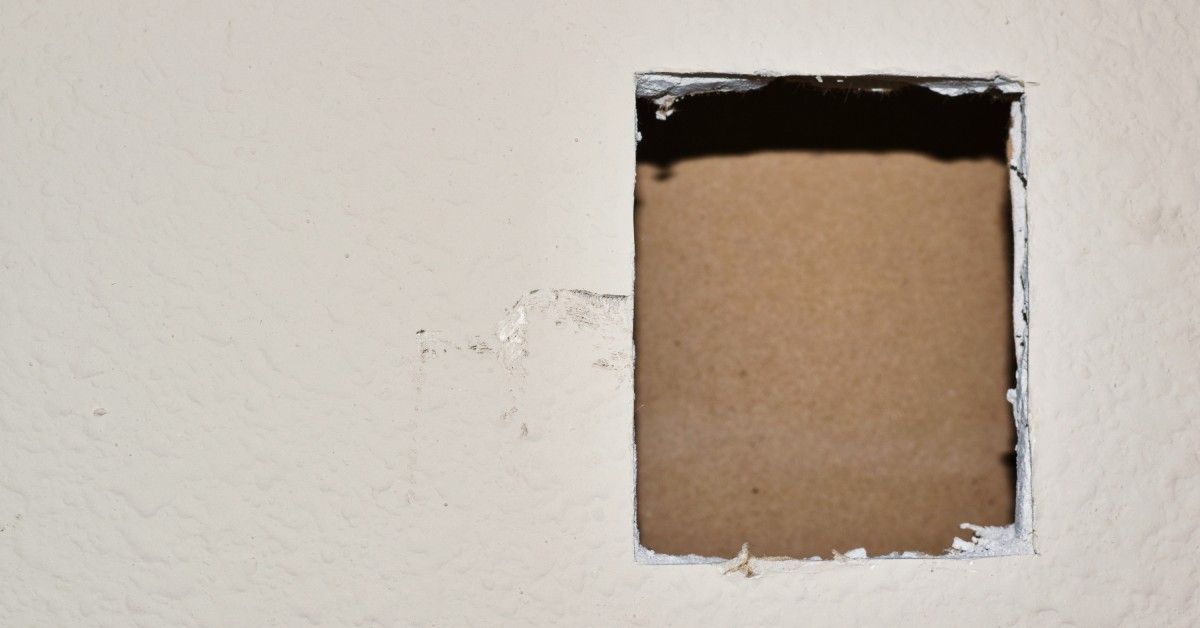 A cut out rectangle in a section of drywall. The walls are cream colored and the cut out is hollow.