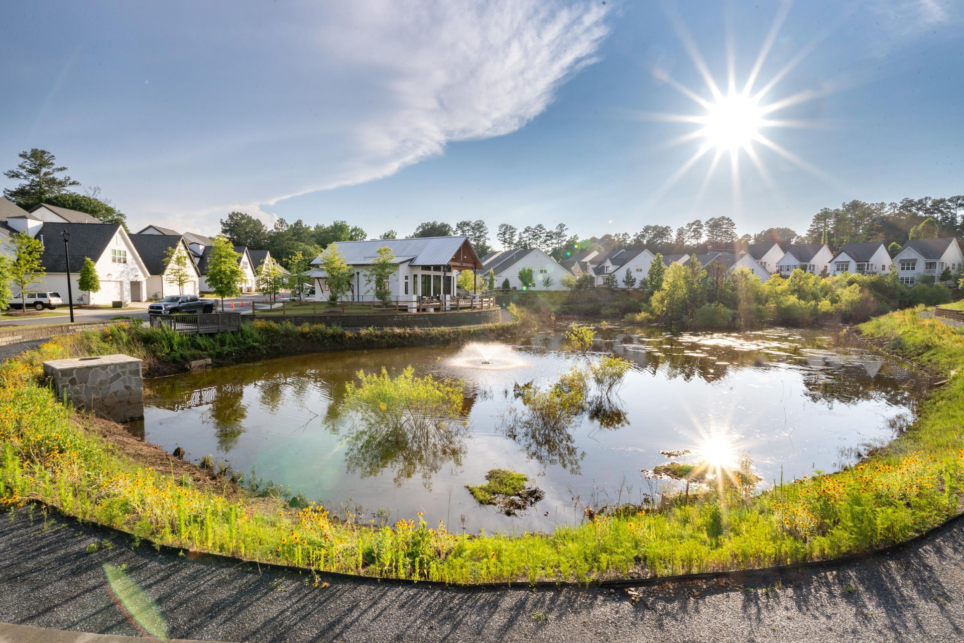 Sunny landscape with a pond in front of houses; sun reflection on water, blue sky.