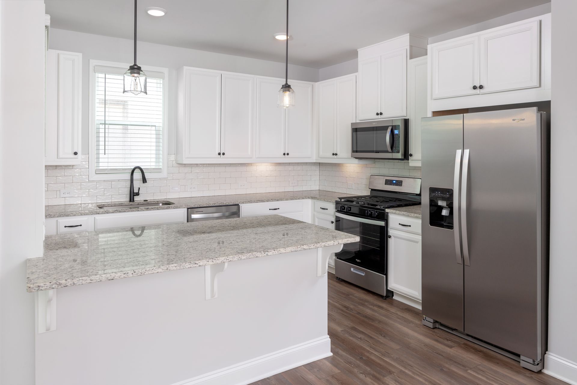 A kitchen with white cabinets , stainless steel appliances , granite counter tops and a refrigerator.