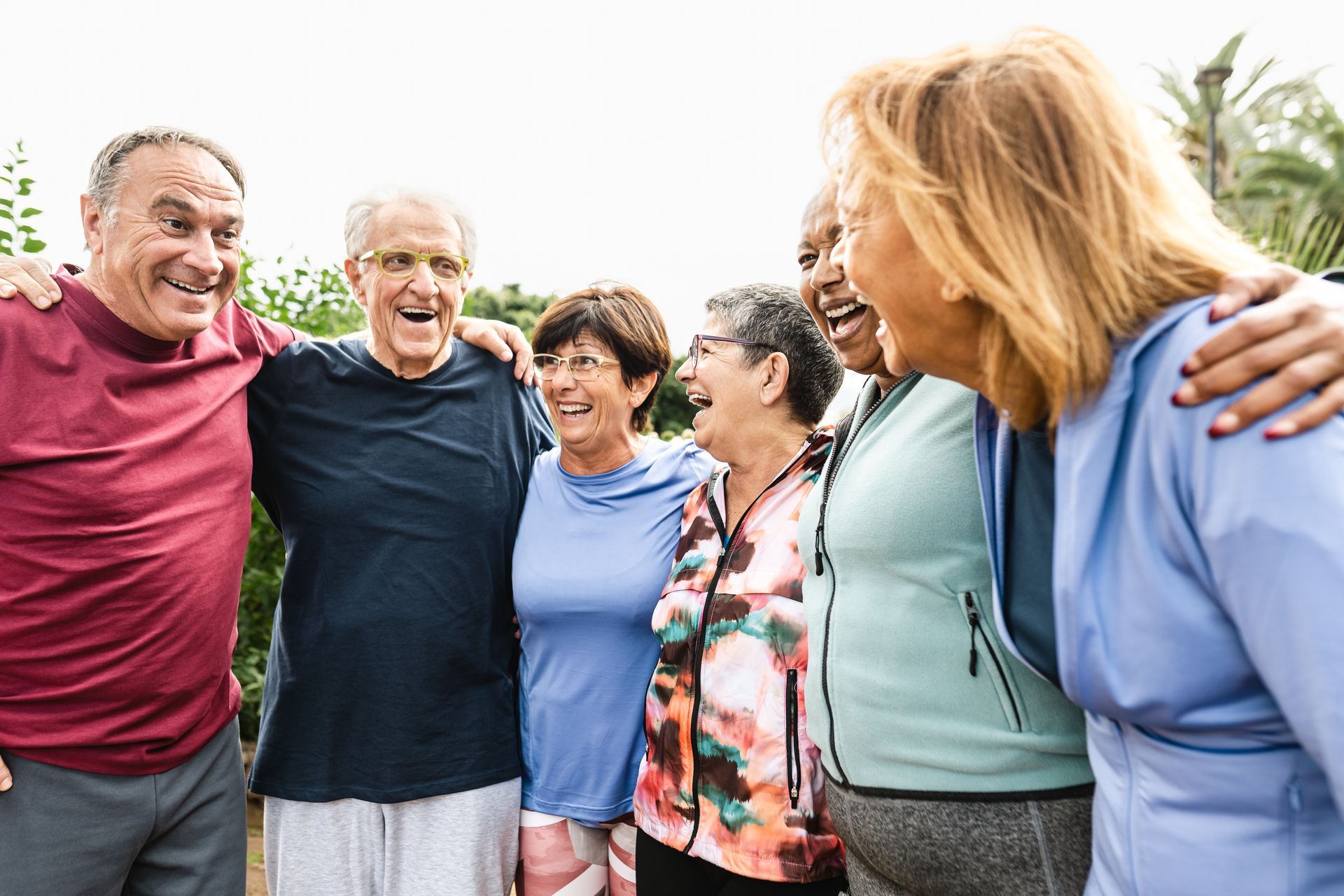 A group of smiling seniors with their arms around each other outdoors, wearing athletic clothing.