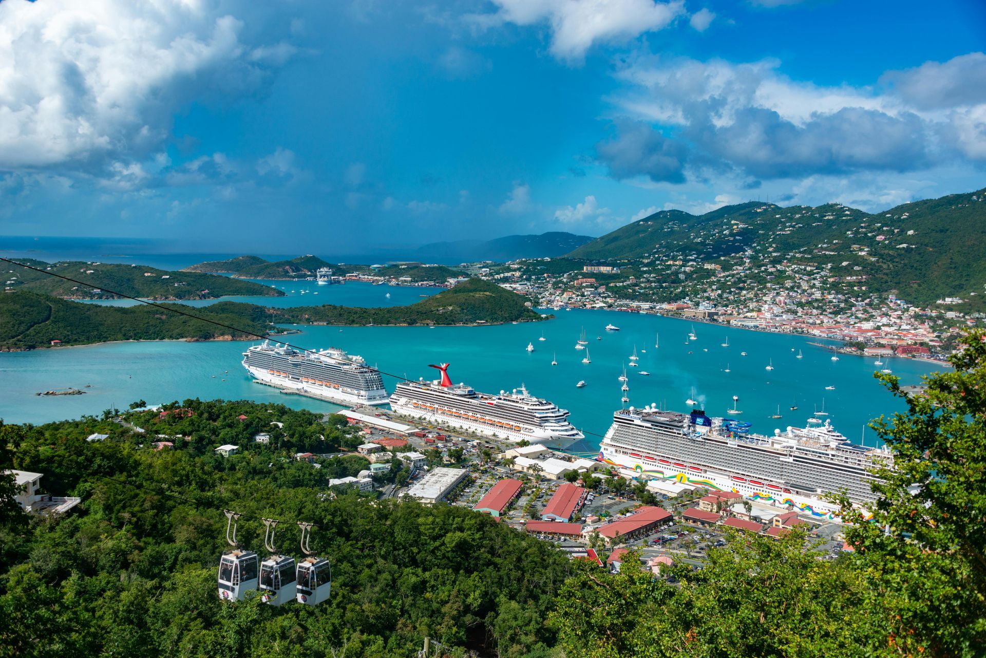 Scenic view of a harbor with cruise ships docked. Hills, blue water, and buildings under a bright blue sky.