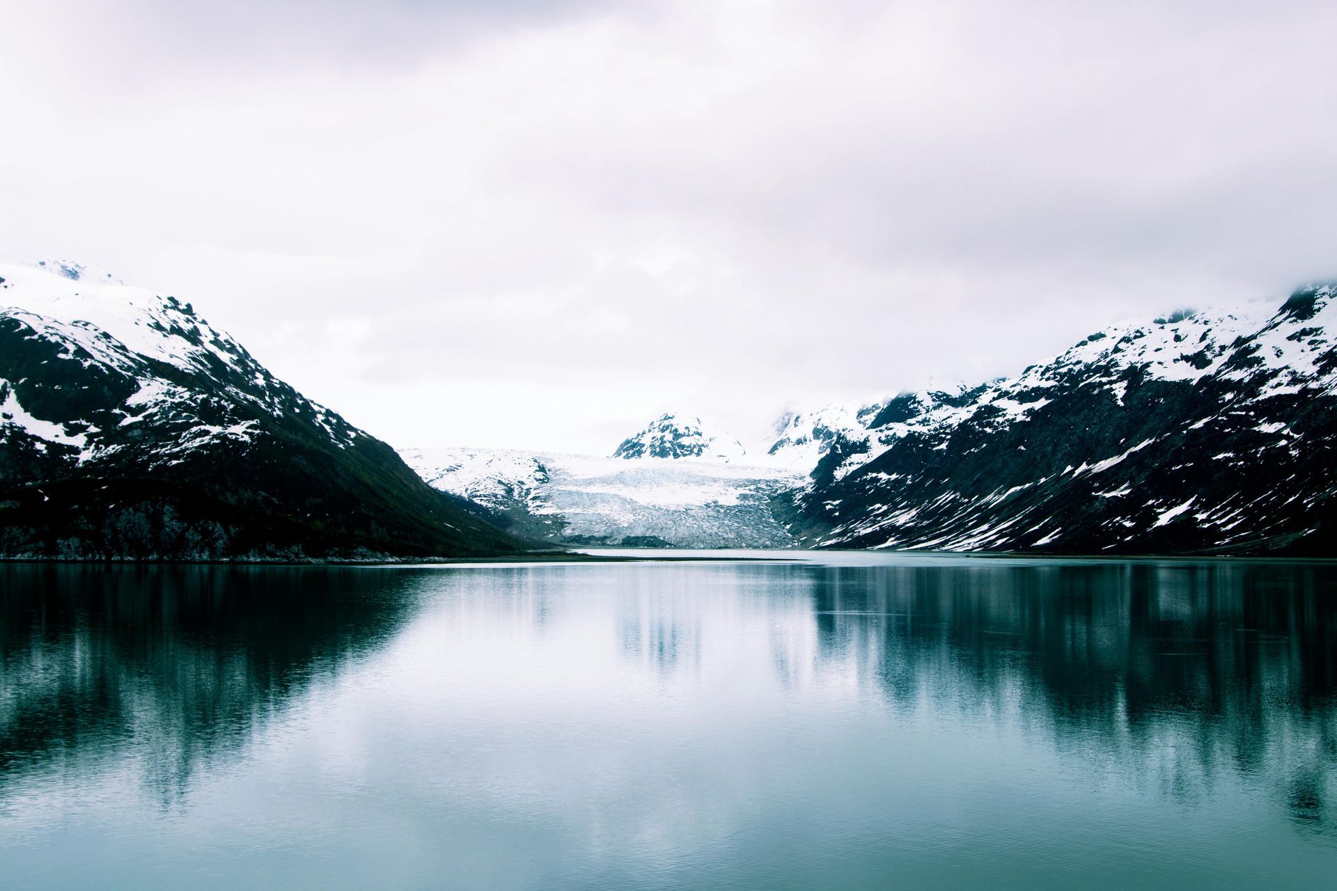 Snow-capped mountains reflected in calm lake water under a cloudy sky.