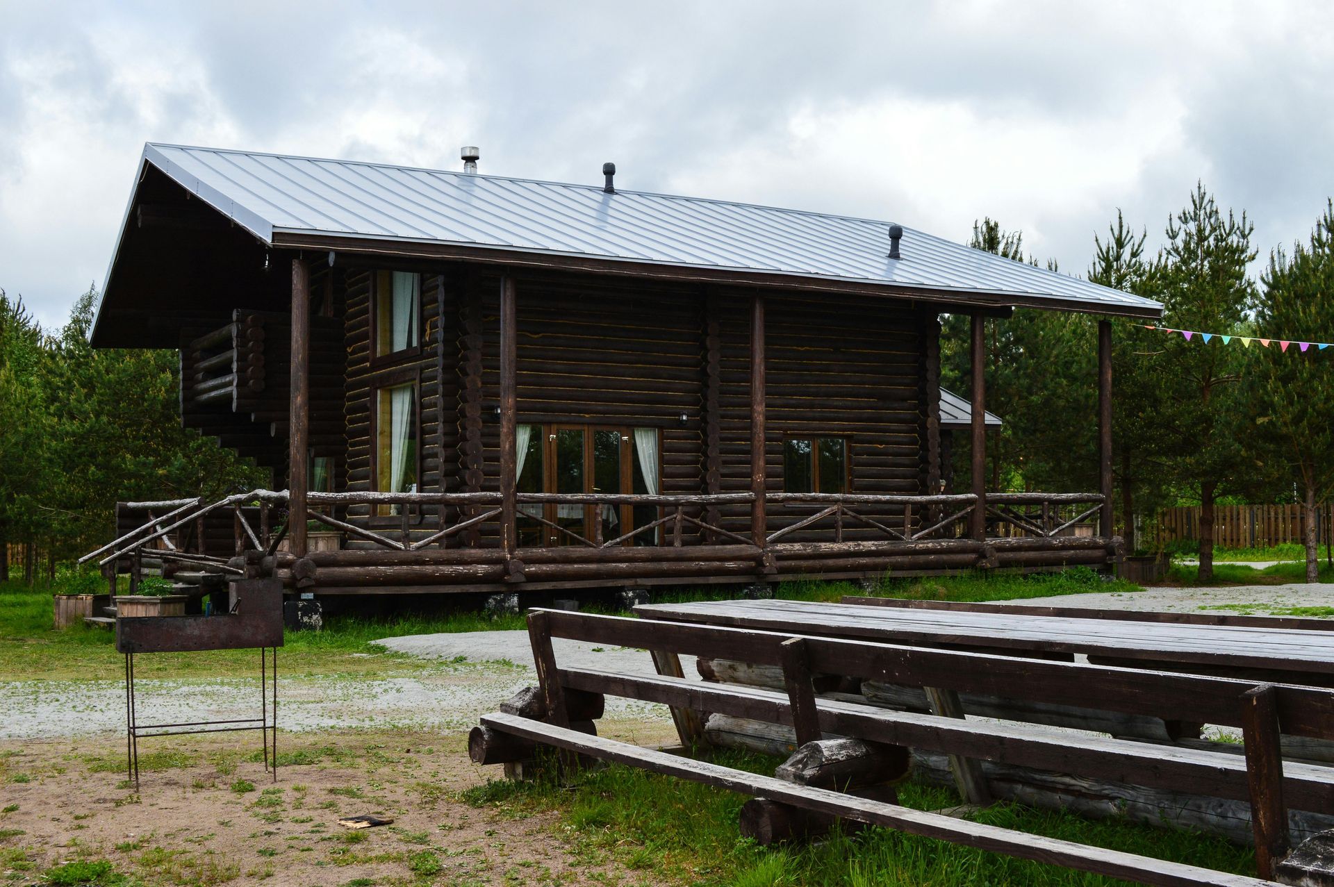 Wooden cabin with metal roof, porch, and picnic table outdoors on a cloudy day.