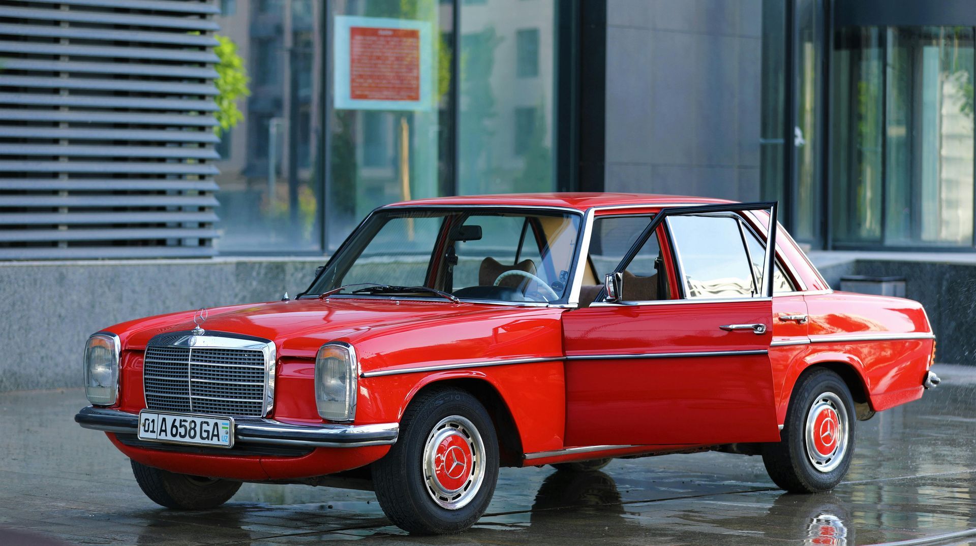 A red vintage Mercedes-Benz sedan parked in front of a building, with the driver's side door open.
