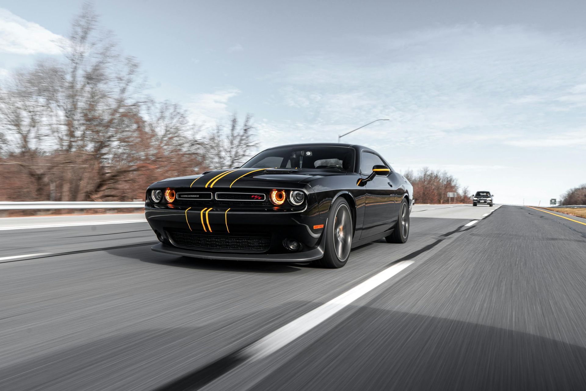 Black Dodge Challenger speeding down a highway, with yellow racing stripes and a blurred background.