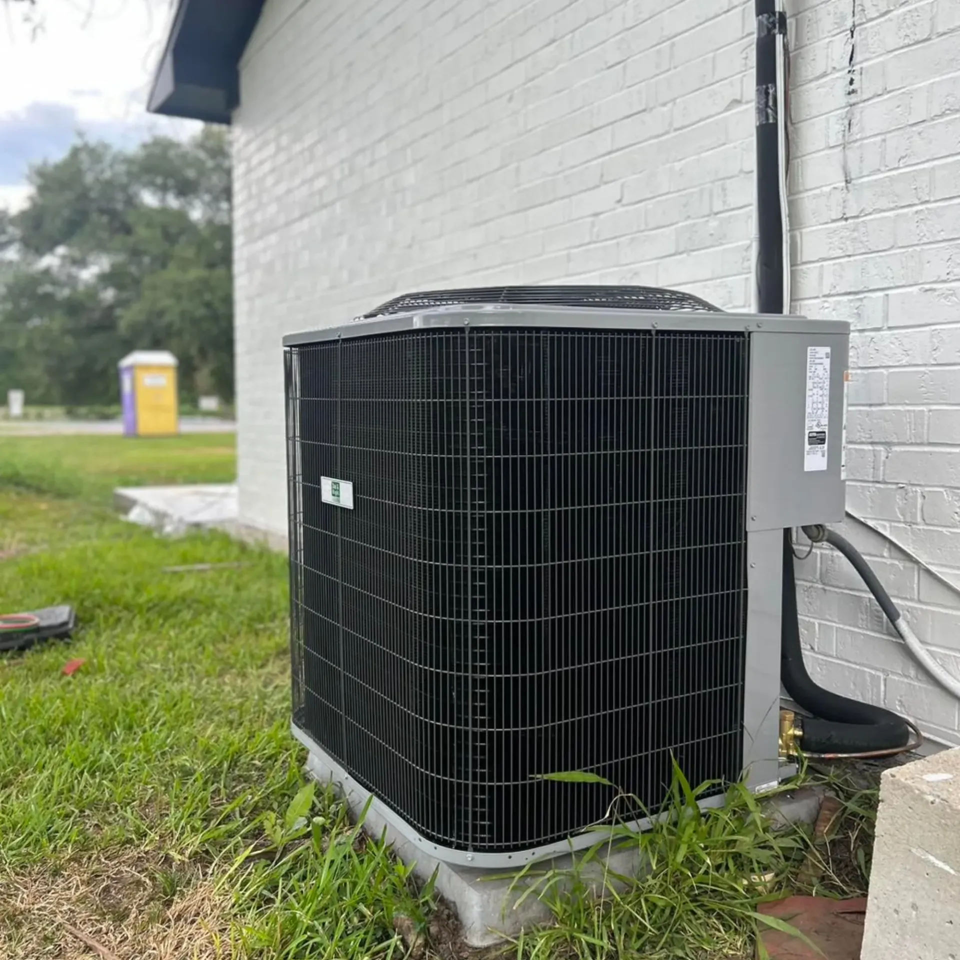 Flawless Heating and Air LLC - A black air conditioner is sitting on the side of a white brick building.