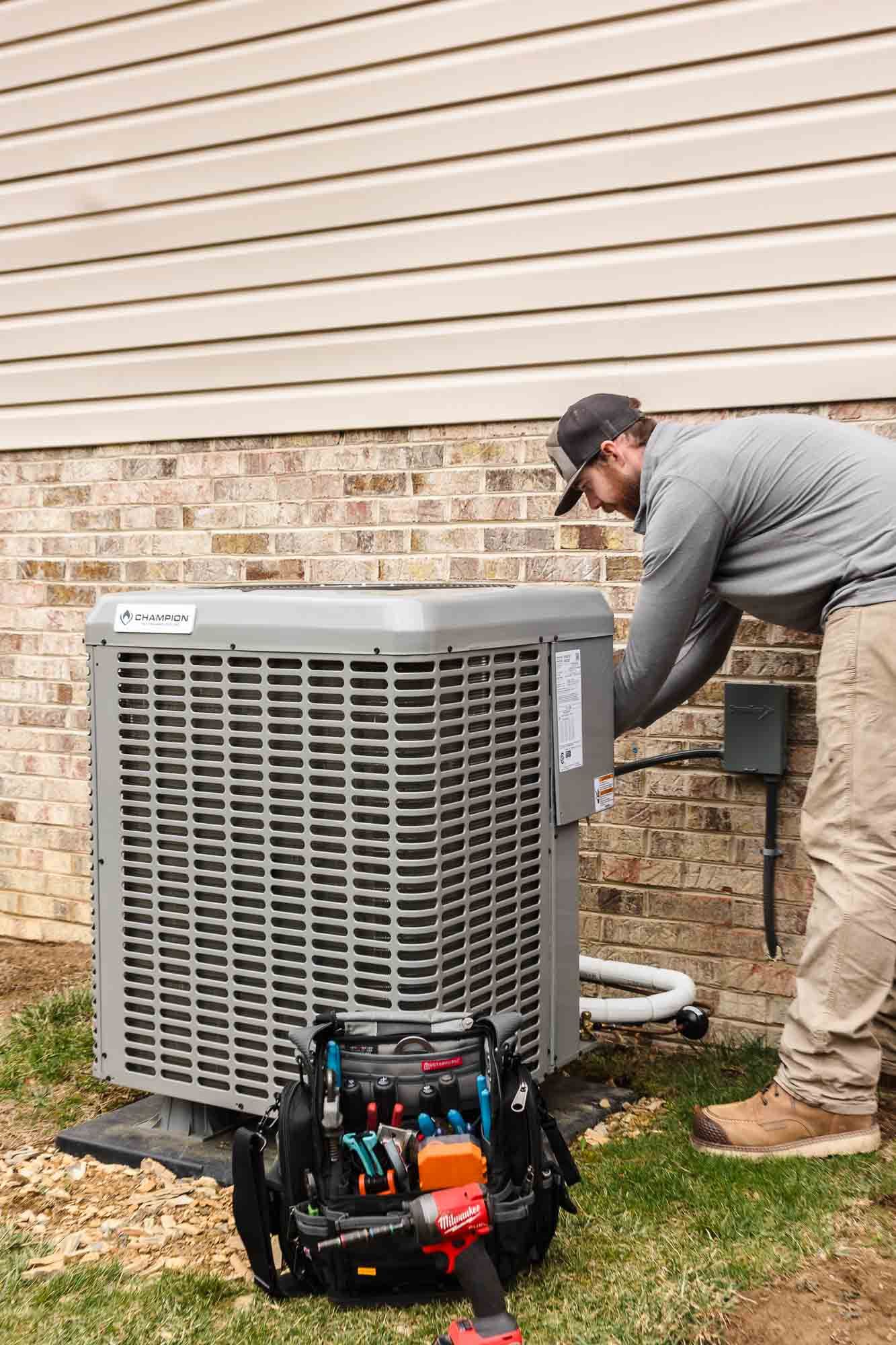 A man is working on an air conditioner outside of a house.