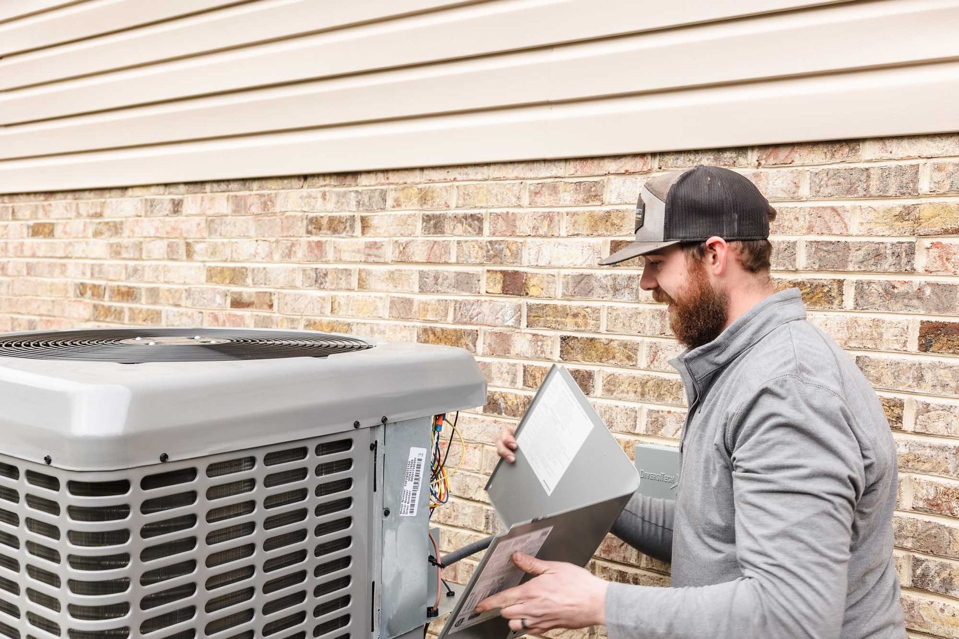 A man is working on an air conditioner outside of a brick building.