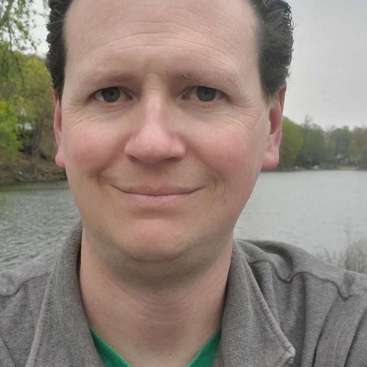 A man is taking a selfie with a lake in the background.