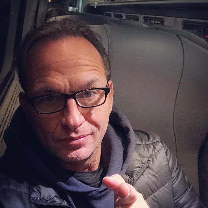 A man wearing glasses is pointing at the camera