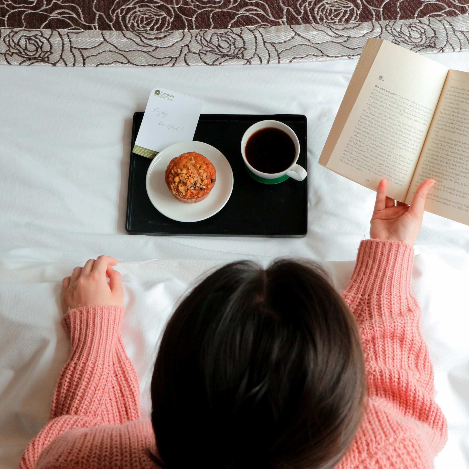 A woman enjoying a cup of coffee and piece of bread while reading during her staycation in Pasig