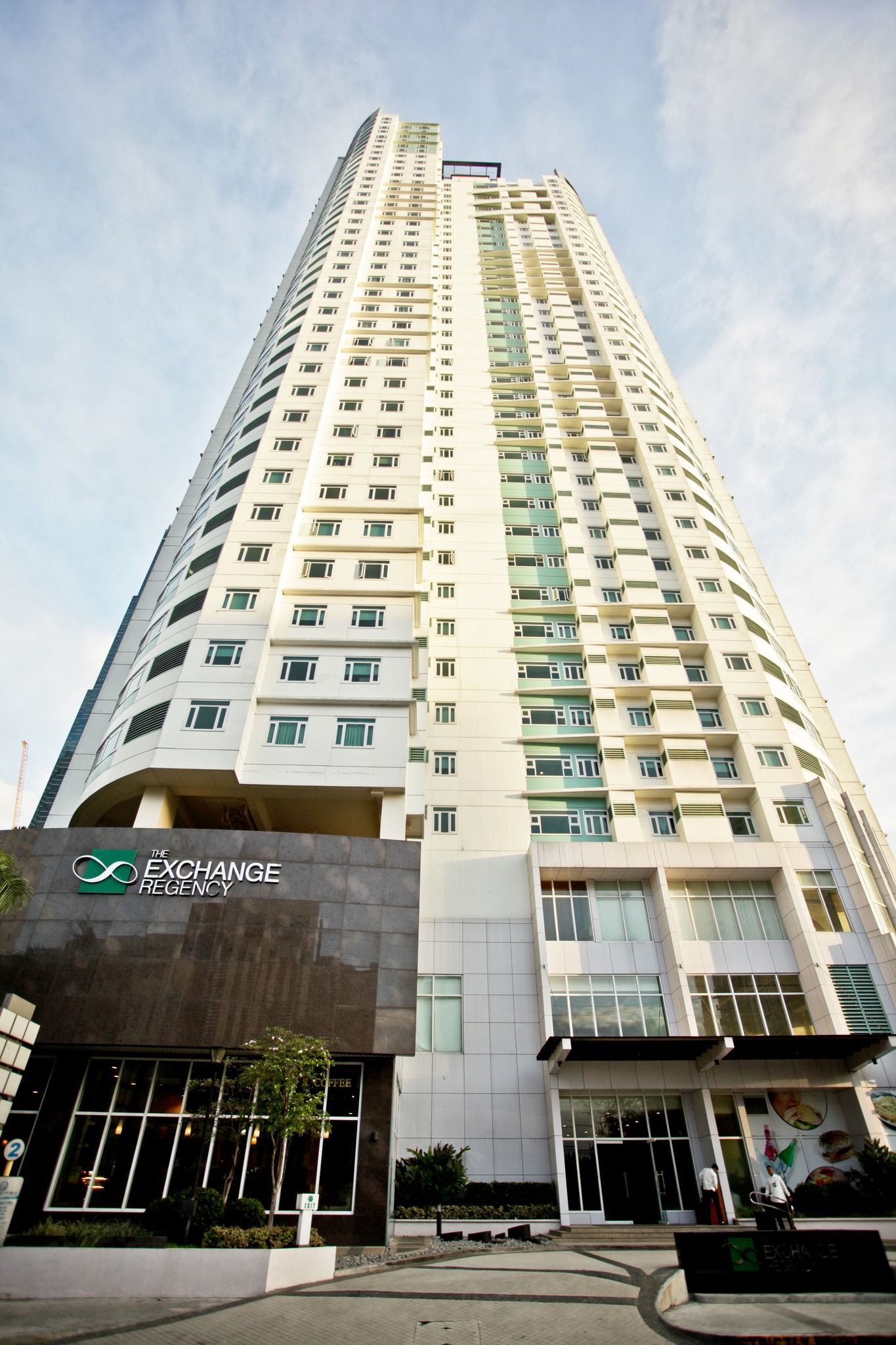 Tall white skyscraper with a dark gray base and green logo, under a cloudy sky.