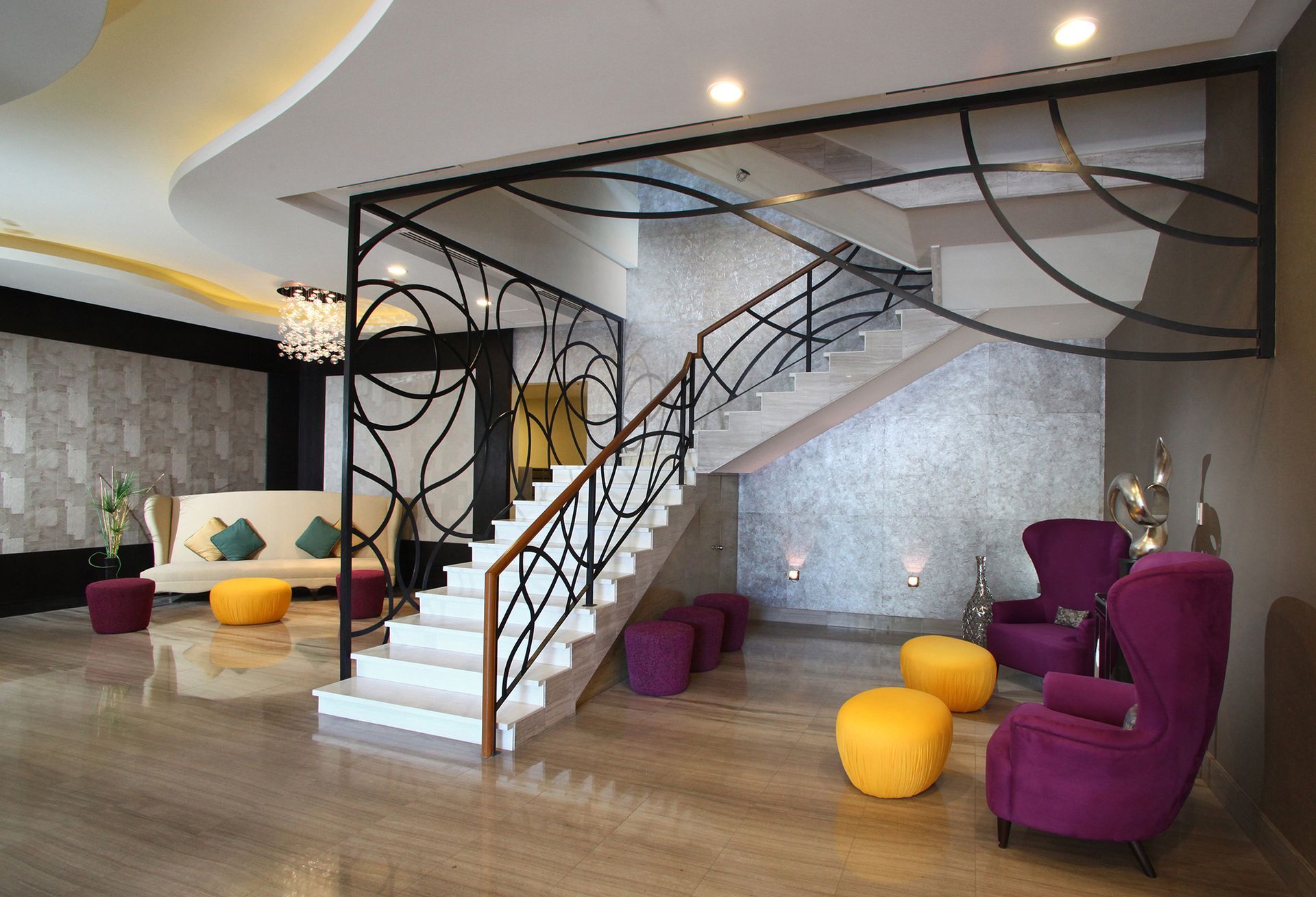 A modern lobby with a staircase, seating, and decorative metalwork. Colors include white, purple, gold, and gray.
