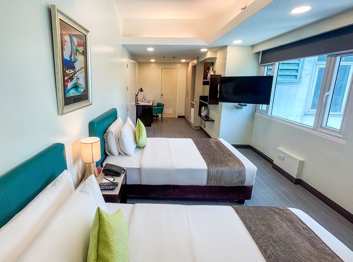 A woman is sitting on a couch looking at her phone and laptop during her staycation in Pasig