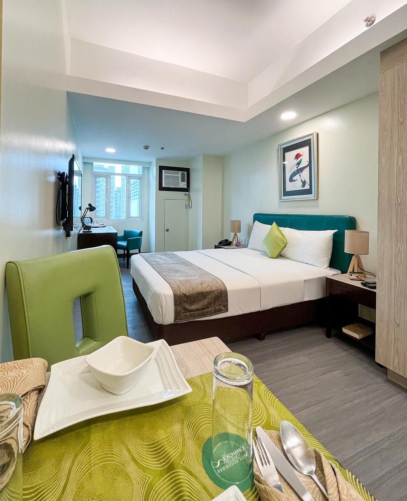 An affordable hotel room with a large bed and a green chair at The Exchange Regency Hotel