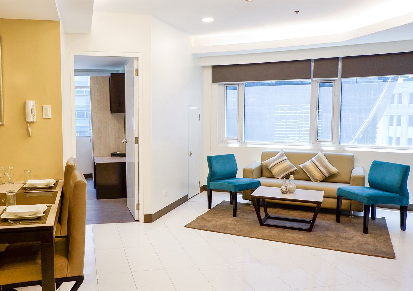 Living room with beige sofa, blue chairs, coffee table, and windows. Dining area visible on left.