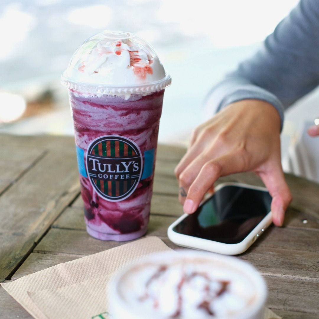 A person is using a cell phone next to a cup of Tully's Cafe beverage