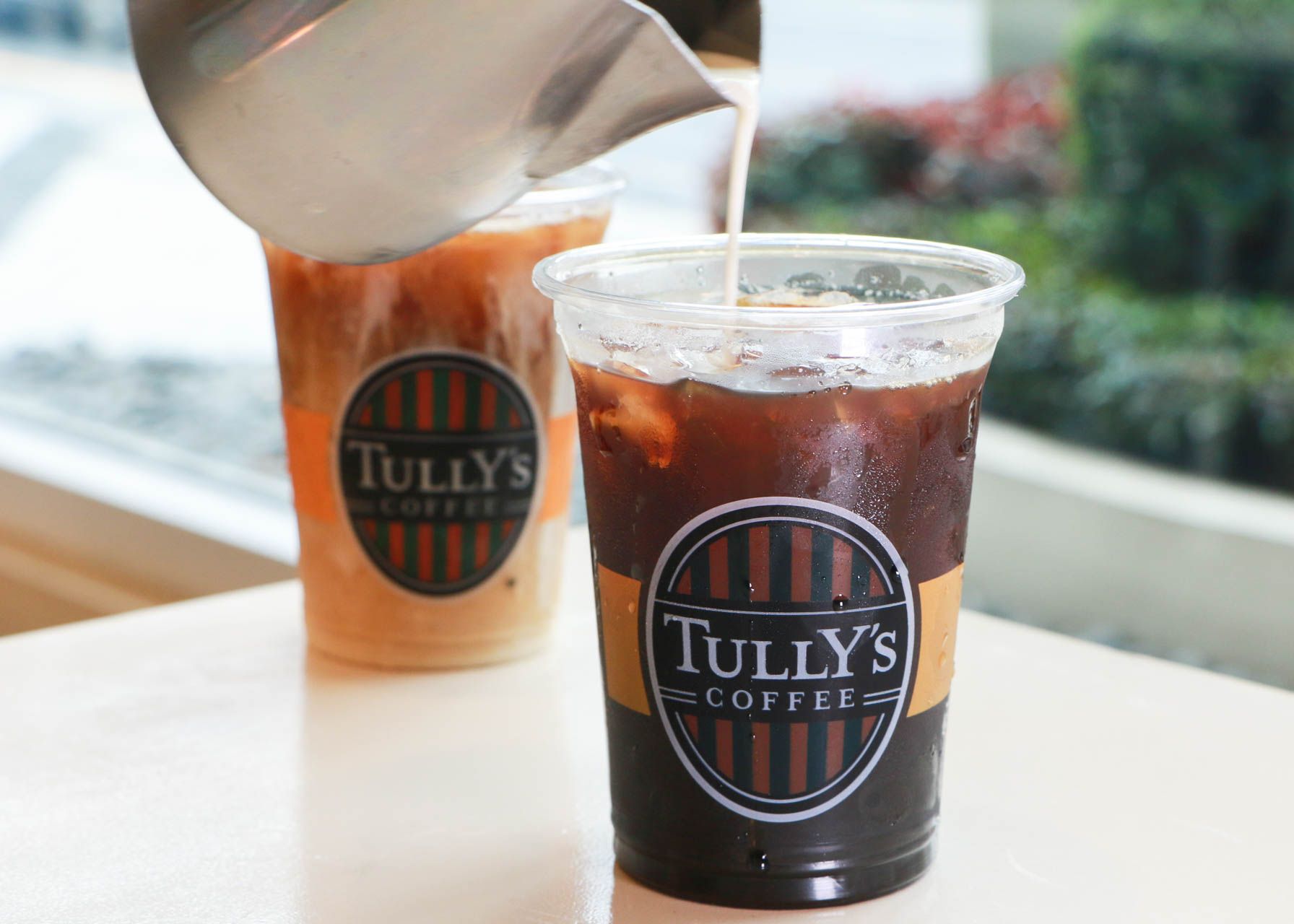 A person is pouring milk into a cup of Tully's coffee.