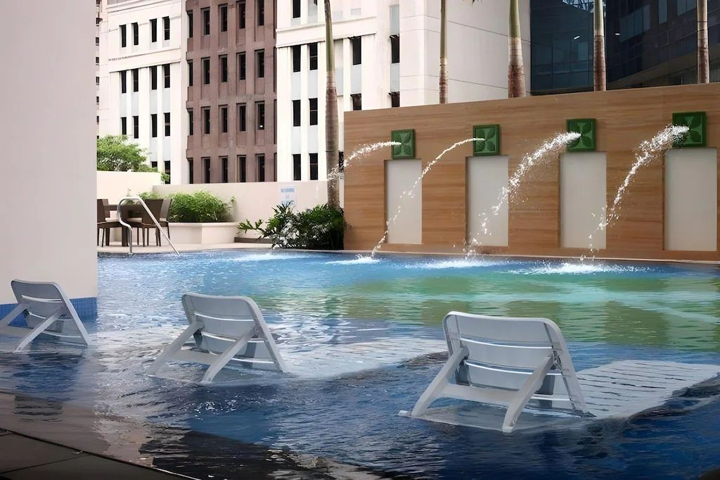 Swimming pool with in-water lounge chairs and water fountains in a hotel near Megamall