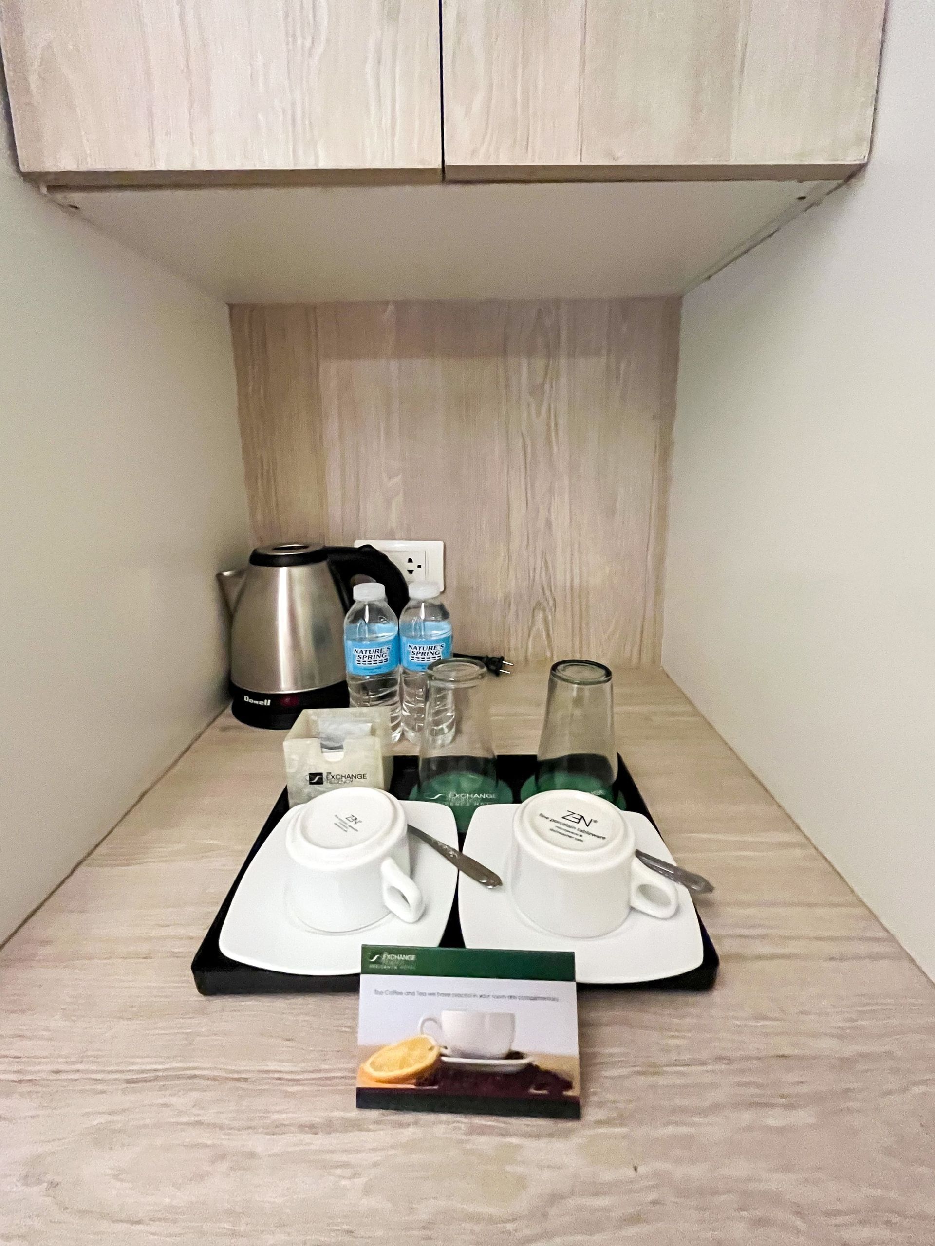 A hotel room with a tray of cups and glasses and a kettle.