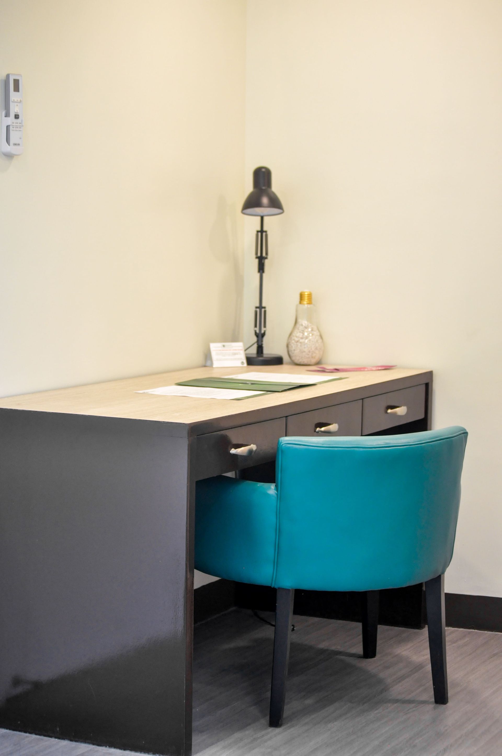 A modern desk with a teal chair, lamp, and decorative items in a corner of a room of a hotel near Megamall