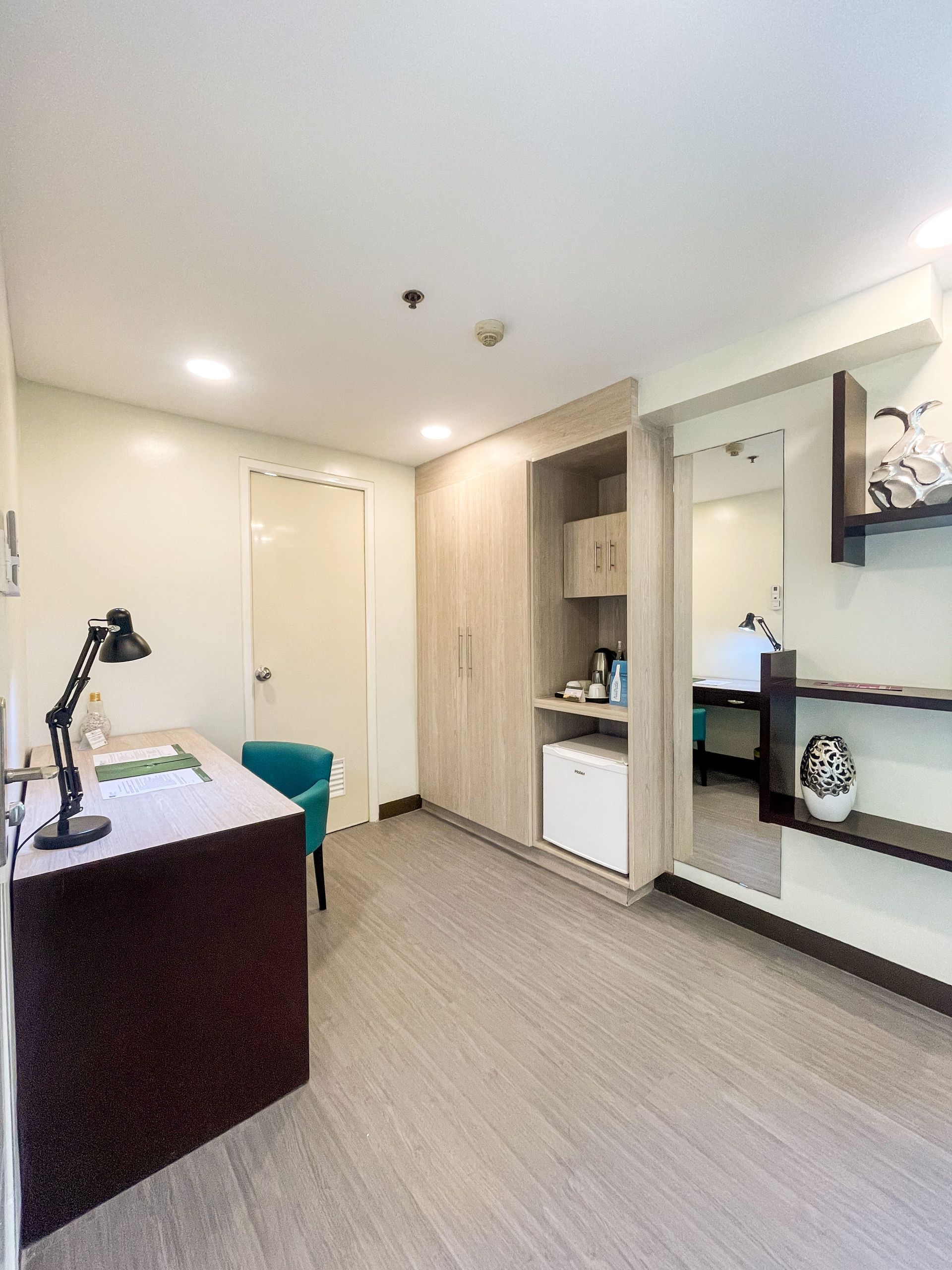 A room with a desk, chair, lamp, and a mirror of a hotel near Megamall