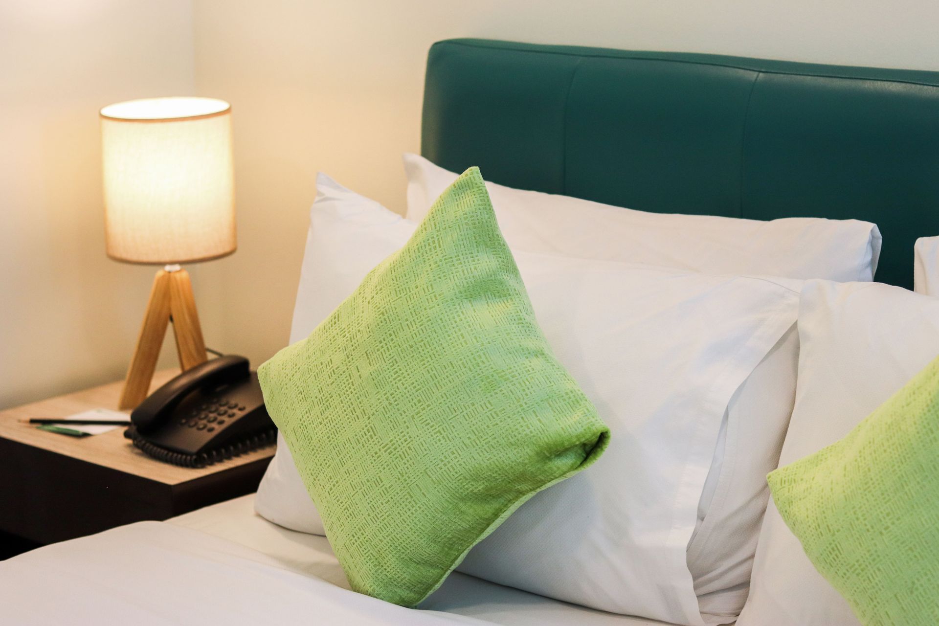 Bed with white bedding, green pillows, and a wooden lamp on the nightstand.