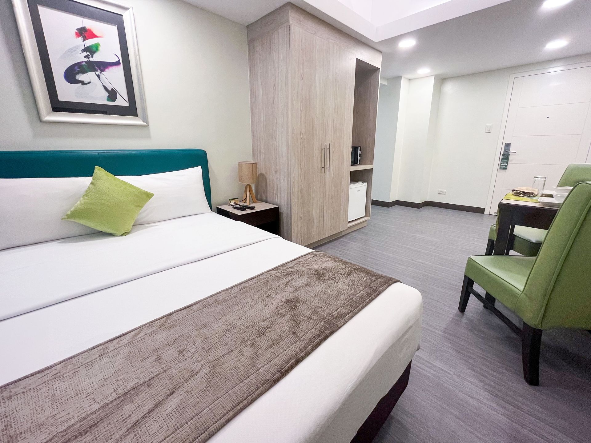 A hotel room with a bed , chair , desk and painting on the wall.