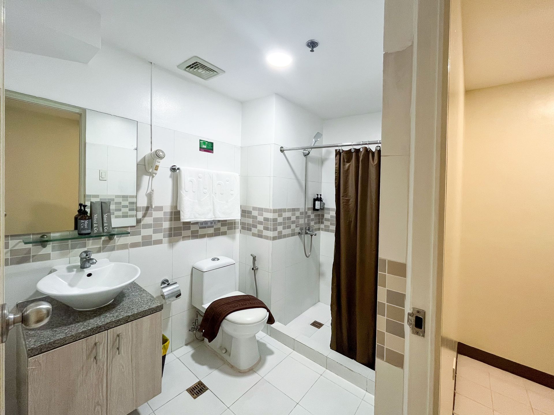 Bathroom with white walls, toilet, sink, and shower with brown curtain.