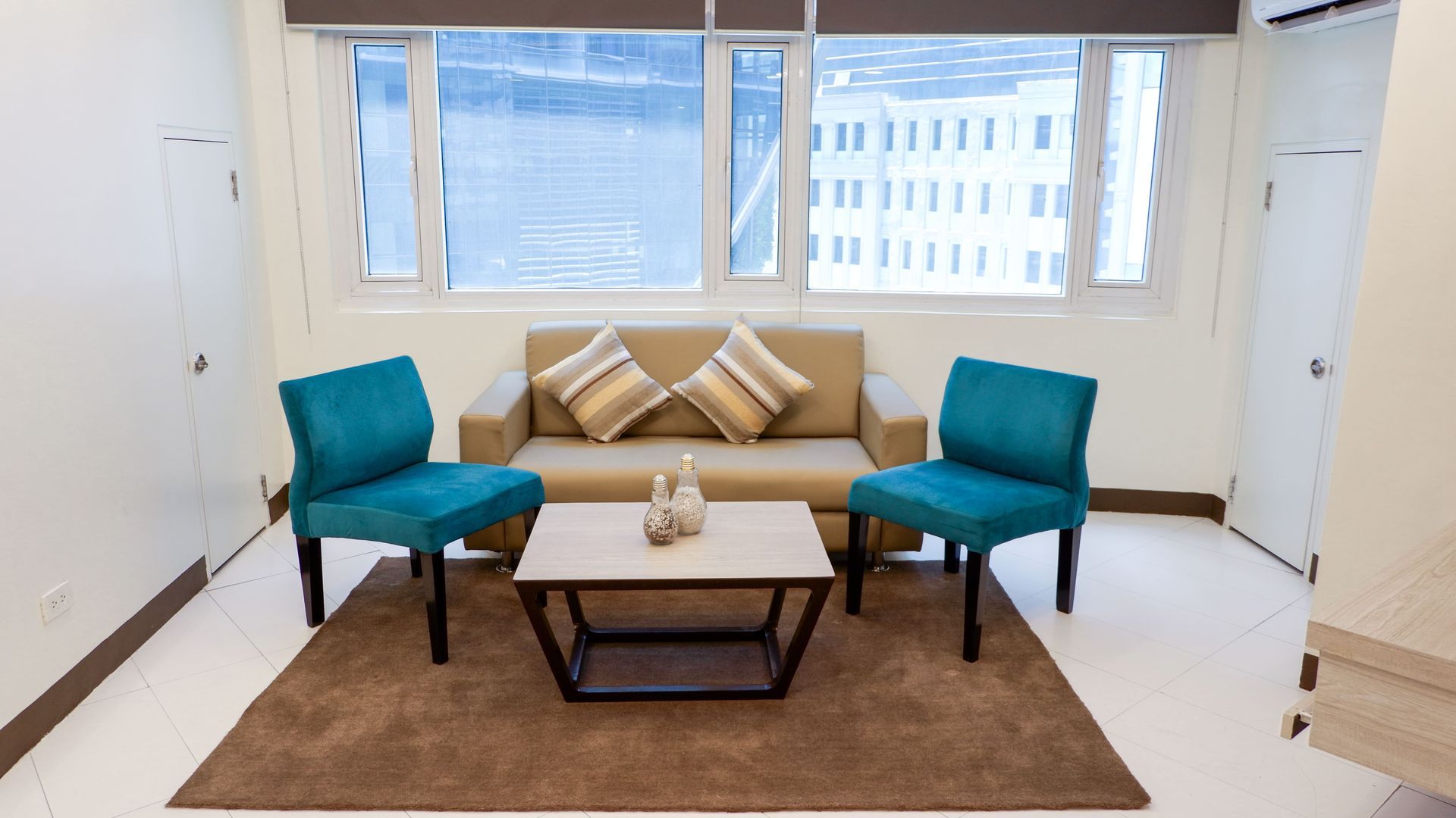 Living room with a tan sofa, two teal chairs, coffee table, and large window at a hotel near SM Megamall