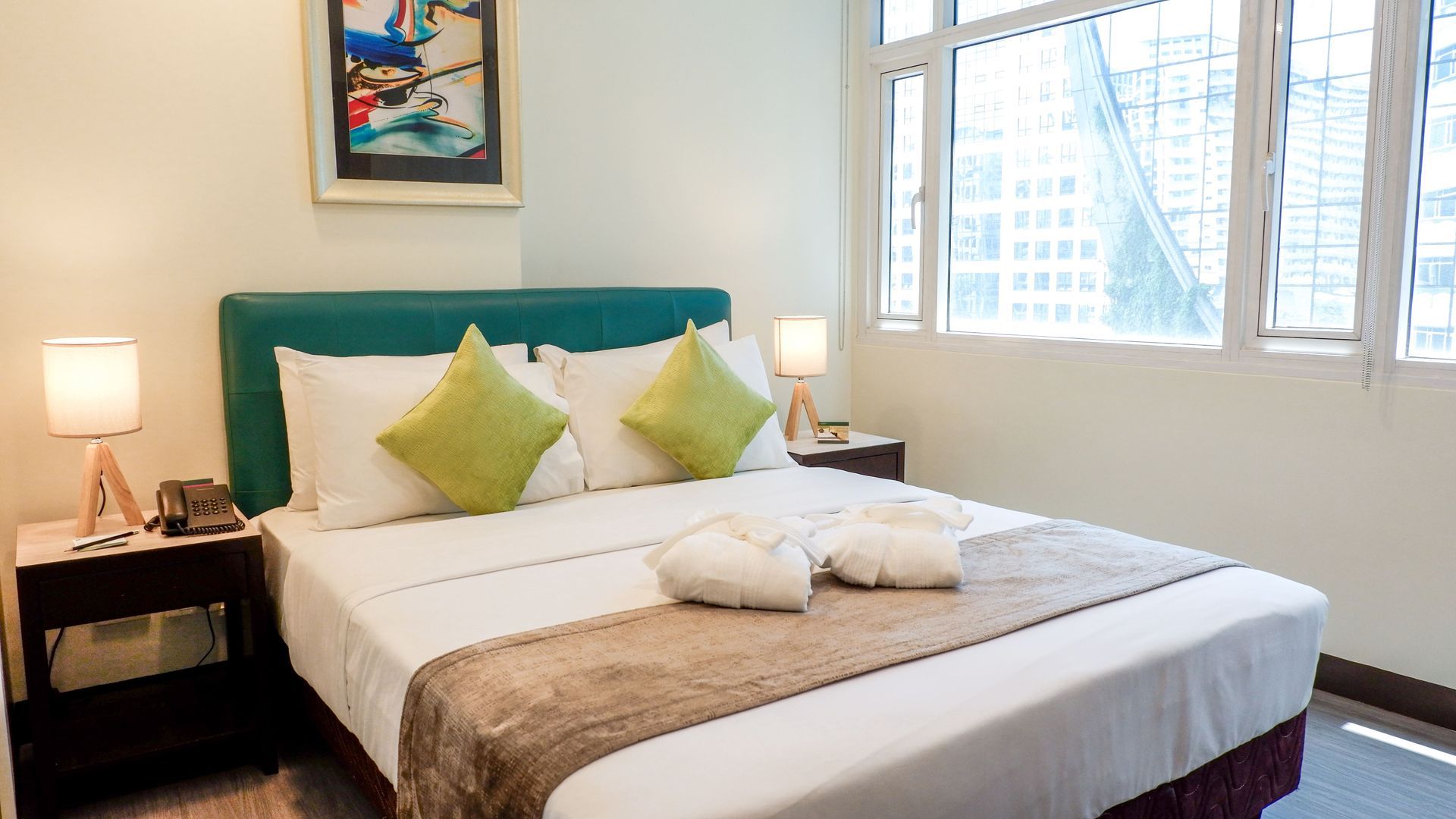 A hotel room with a bed , two lamps , a picture on the wall and a window.