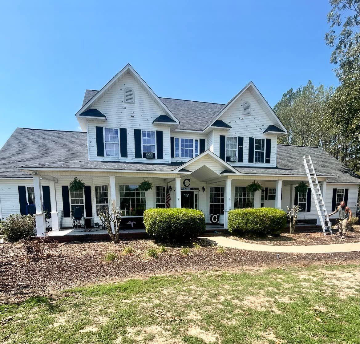 A large white house with black shutters and a ladder in front of it.