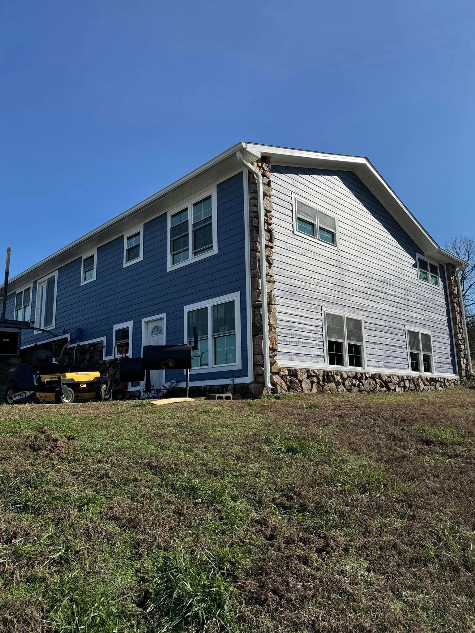 Two-story house with blue siding, white trim, and stone accents under a clear, blue sky.
