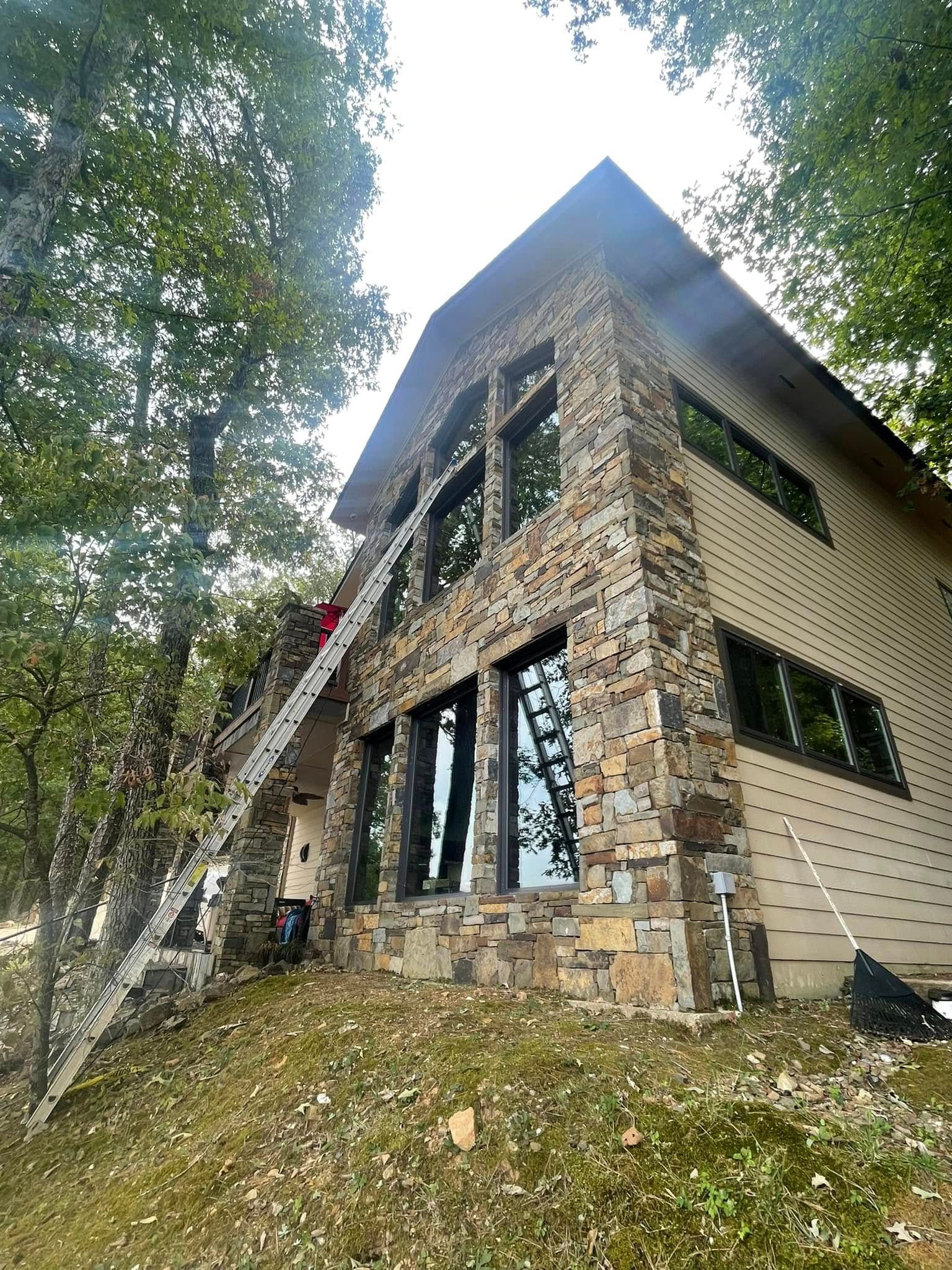 A man is standing on a ladder in front of a large stone house.