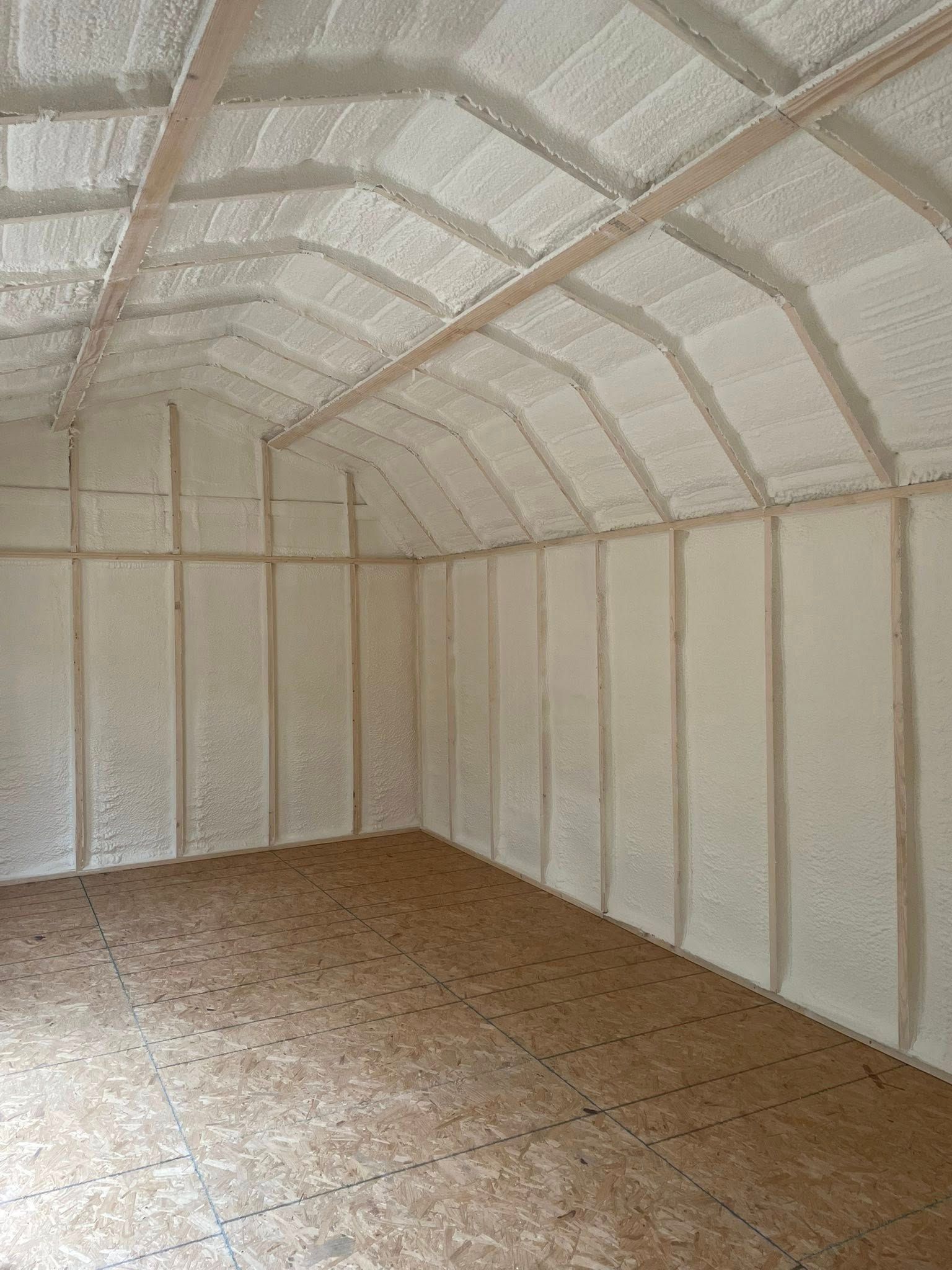 Interior of a building with exposed wood framing and walls and ceiling insulated with white foam.