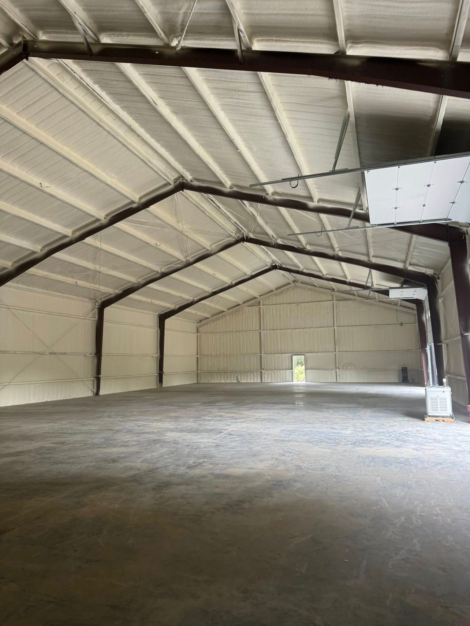 Empty warehouse interior, gray concrete floor, white spray foam insulation, steel beams.