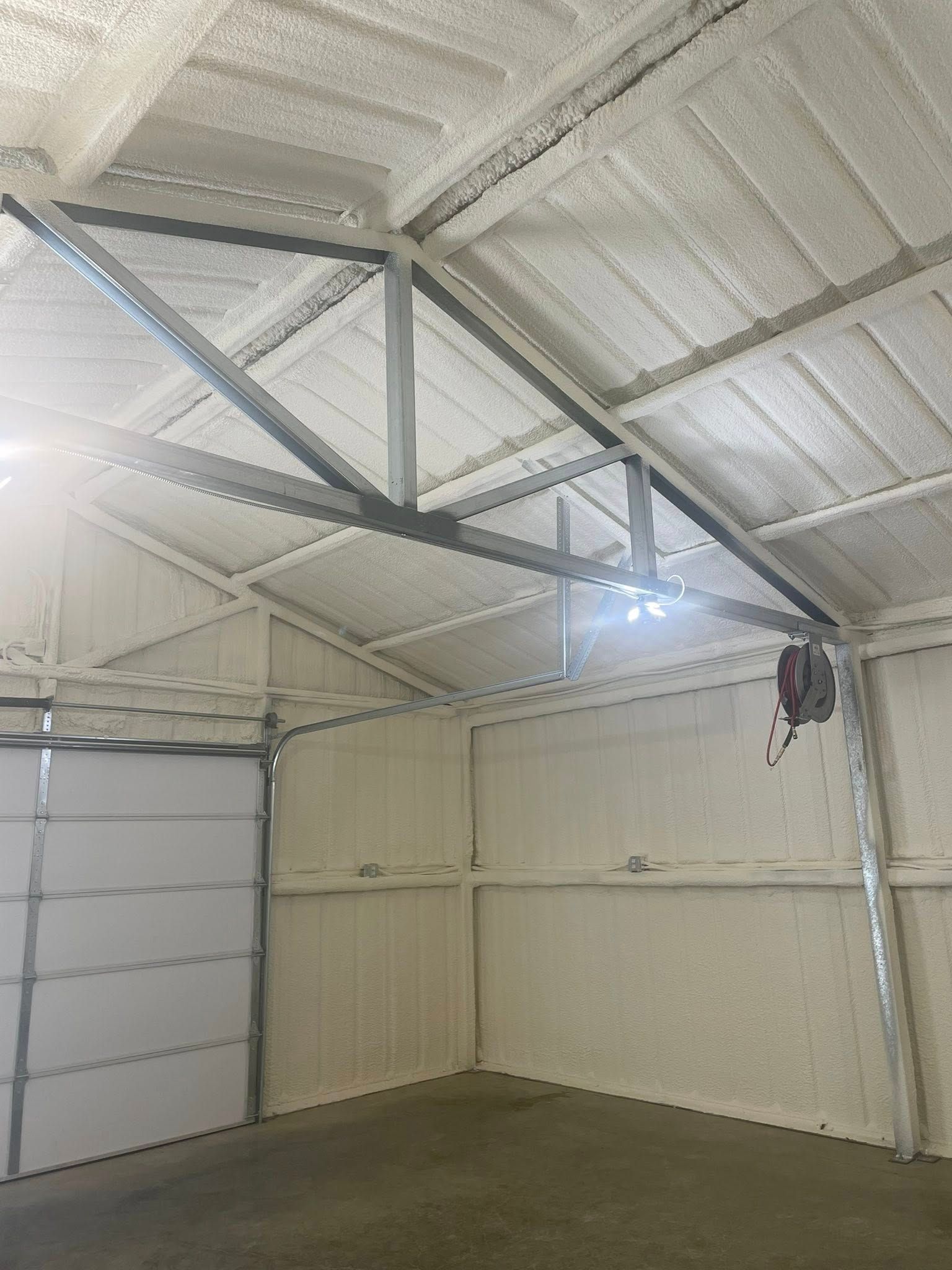 Interior of a metal building with spray foam insulation on the walls and ceiling. A garage door is on the left.