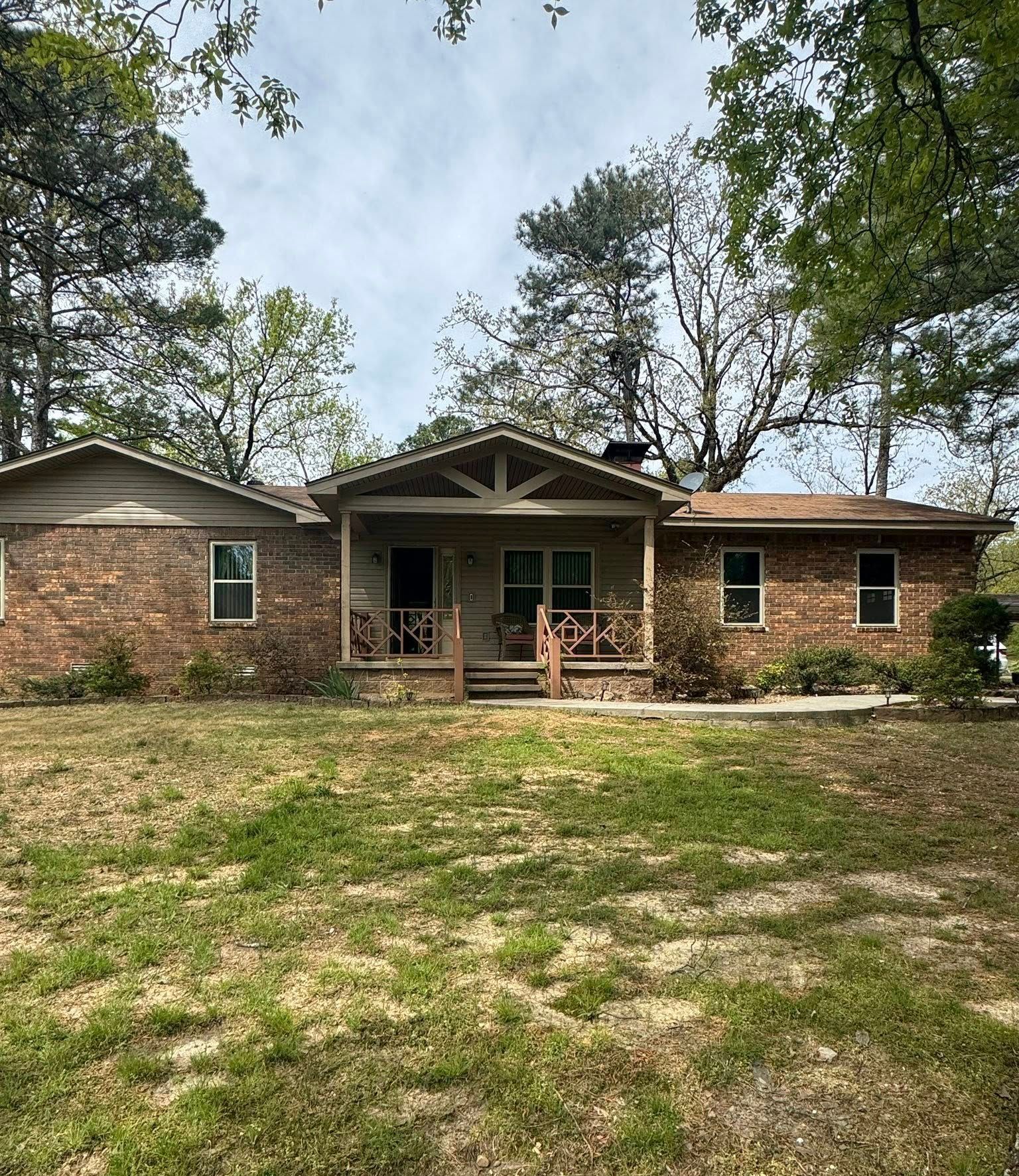 Brick ranch-style house with a covered porch; green lawn, trees in background, overcast sky.